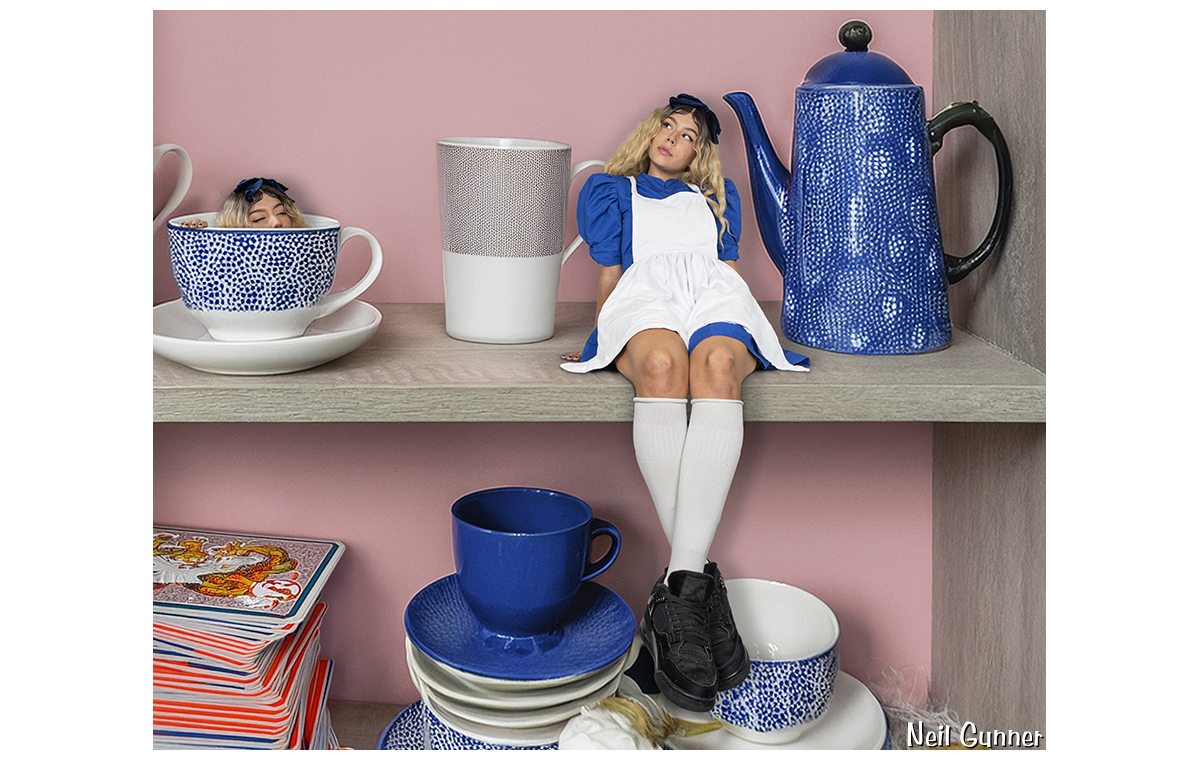 Tiny Alice sits on a shelf amidst tea cups, with a second Alice hiding in a cup